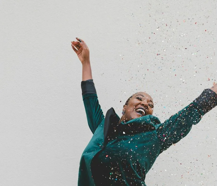 A woman leaping with her arms up as confetti falls around her.