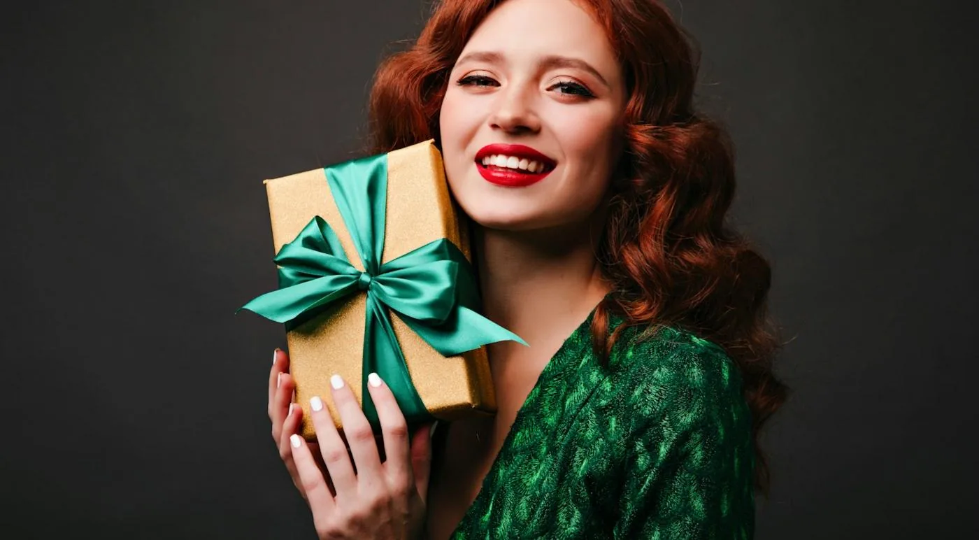 A smiling woman holding a wrapped gift to her cheek.