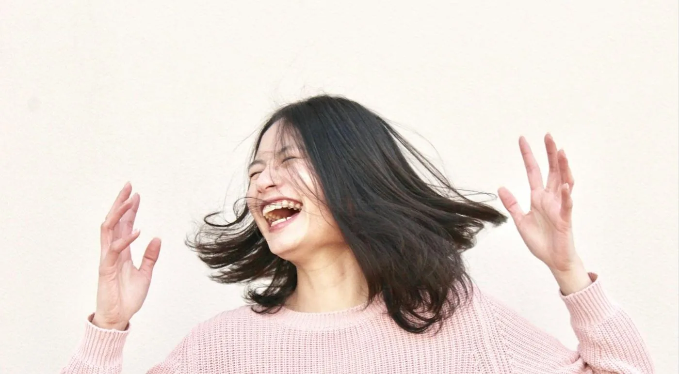 A woman laughing and tossing her hair, hands raised.